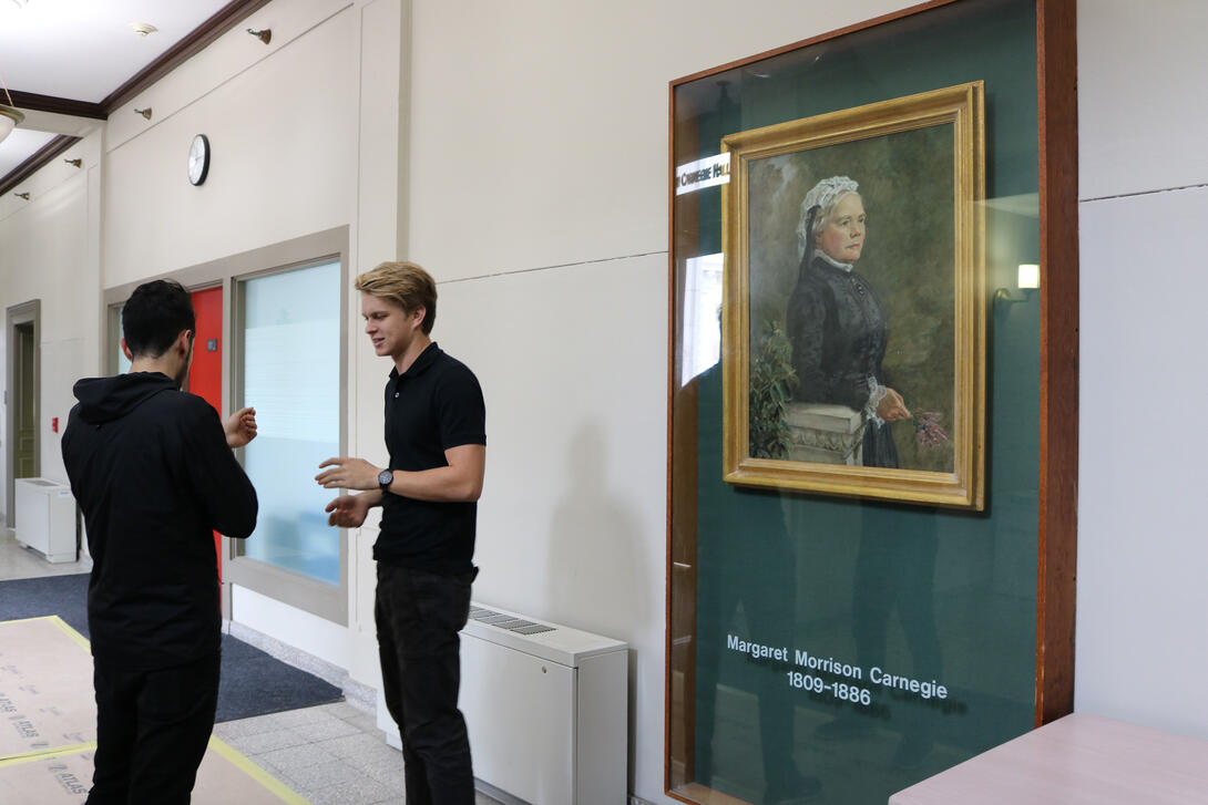 Two students talking in front of the portrait of Margaret Morrison.